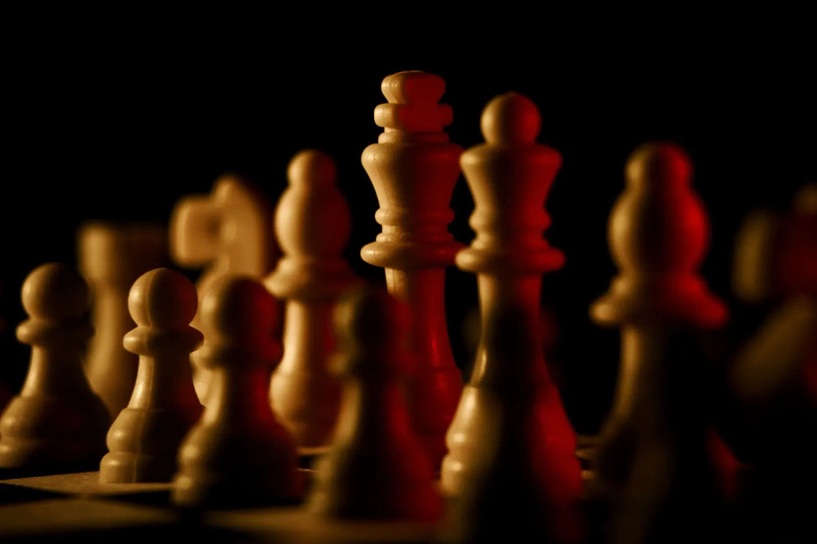 Wooden chess pieces lit warmly against a dark background, the king standing tallest